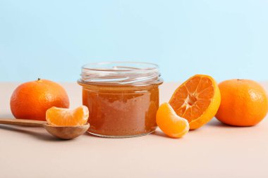 Jar of sweet tangerine jam on color background