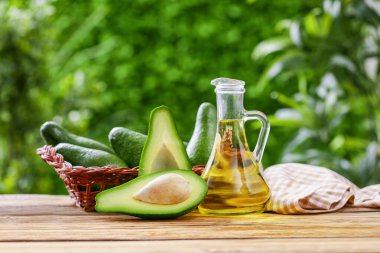 Dışarıdaki ahşap masada avokado bulunan bir sürahi taze yağ ve hasır sepet.