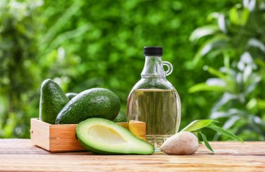 Dışarıdaki ahşap masada bir şişe taze yağ ve avokado.
