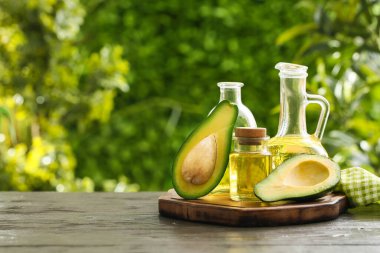 Şişeler ve sürahi taze avokado yağı açık havada, siyah ahşap masada.