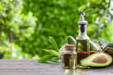 Şişeler dolusu taze yağ ve hasır sepet ve açık havada siyah ahşap masa üzerinde avokadolar.