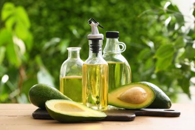 Dışarıdaki bej ahşap masada taze avokado yağı şişeleri.