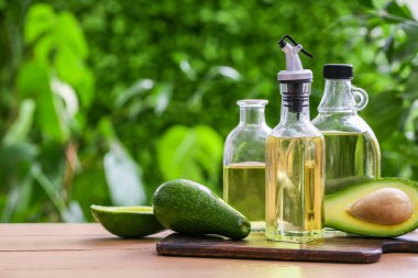 Dışarıdaki bej ahşap masada taze avokado yağı şişeleri.