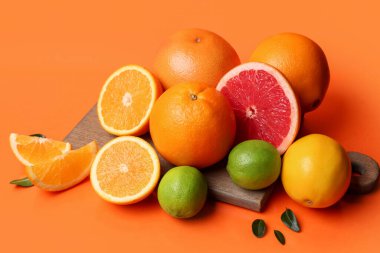 Farklı kesilmiş turuncu meyveli ahşap tahta ve turuncu arka planda yapraklar.