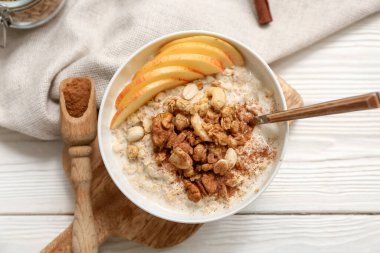 Lezzetli yulaf ezmeli kompozisyon, beyaz ahşap arka planda elma ve fındık parçaları.