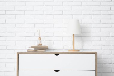 İçinde lamba olan çekmeceler ve beyaz tuğla duvarın yanında kitaplar.