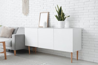 Oturma odasındaki gri kanepenin yanında saksısı olan çekmeceler.