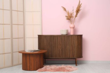 Oturma odasındaki ahşap masanın yanında vazo olan çekmeceler.