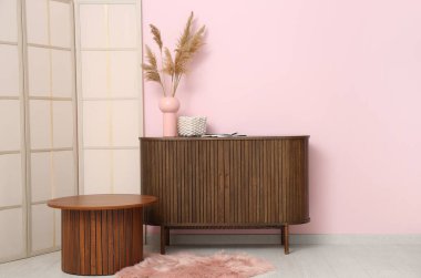 Oturma odasındaki ahşap masanın yanında vazo olan çekmeceler.