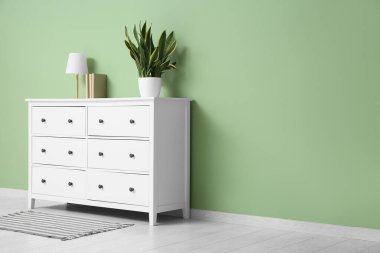 Oturma odasında lamba ve çiçek olan beyaz çekmeceler.