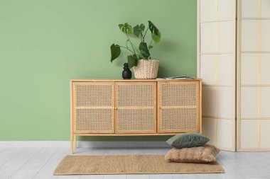 Oturma odasındaki perdenin yanında saksı olan ahşap çekmeceler.