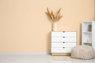 Oturma odasındaki rafların yanında beyaz çekmeceler ve yumuşak puf.