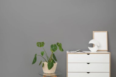 Çerçeveli beyaz çekmeceler ve gri duvarın yanında dergiler.