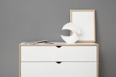 Çerçeveli beyaz çekmeceler ve gri duvarın yanında dergiler.