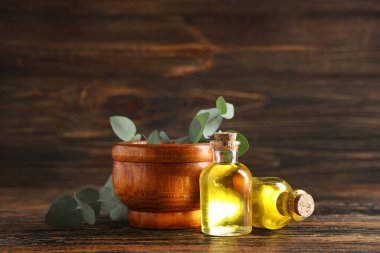 Mortar with eucalyptus branches and bottles of essential oil on wooden background