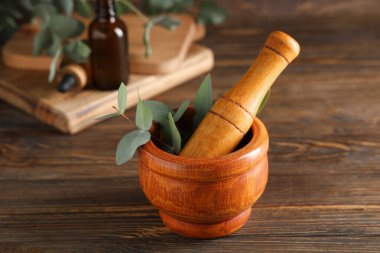 Mortar and pestle with eucalyptus branches and bottle of essential oil on wooden background