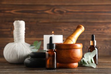 Mortar and pestle with eucalyptus branches, bottles of essential oil and spa supplies on wooden background