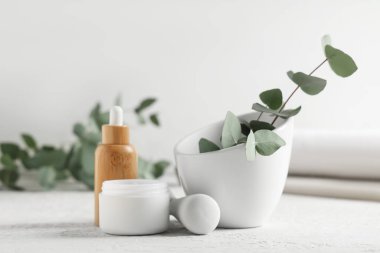 Mortar and pestle with eucalyptus branches, jar of cosmetic cream and bottle of essential oil on white background