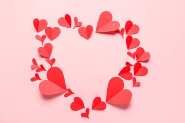 Pembe arka planda kırmızı kağıt kalplerden yapılmış bir çerçeve. Sevgililer Günü kutlaması