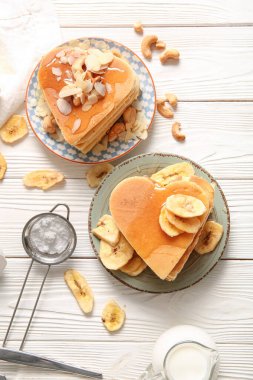 Kalp şeklinde lezzetli gözlemeler, hafif ahşap arka planda kurutulmuş muz ve fındıklar. Sevgililer Günü kutlaması