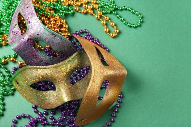 Mardi Gras kutlamaları için boncuklu parlak karnaval maskeleri yeşil arka planda.