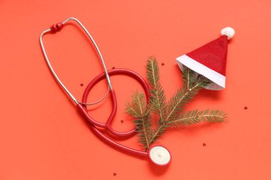 Noel ağacı dalları ve kırmızı arka planda Noel Baba şapkası olan steteskop