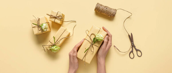 Руки женщины с подарочными коробками ручной работы и красивыми белыми розами на бежевом фоне, вид сверху