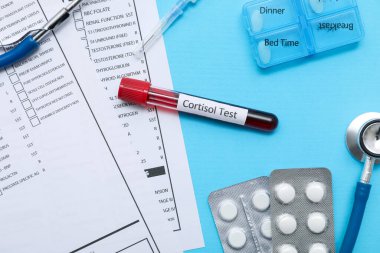 Laboratuvar test formları, steteskop ve mavi arka planda haplı kortizol örneği, yakın plan. Tıbbi konsept