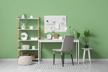 Yeşil duvarda raf ünitesi ve tahta olan şık bir iş yeri.