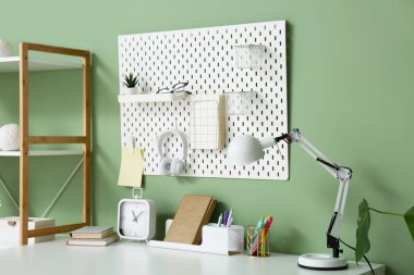 Renk duvarında kırtasiye, lamba, alarm saati ve tahta bulunan modern iş yeri