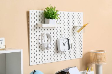 Çalar saati, modern kulaklıkları, kırtasiyesi ve renkli duvarda asılı bitkisi olan tahta.