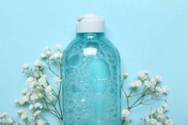 Bir şişe mikiler suyu ve mavi arka planda çiçekler.