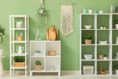 Mutfağın içinde temiz bulaşık takımları ve ev bitkileri olan raflar.