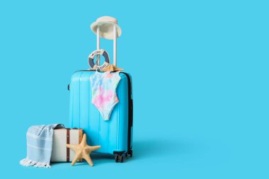 Çocuk mayolu bavullar ve mavi arka planda plaj aksesuarları.