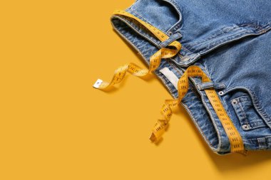 Sarı arka planda ölçü bandı olan kot pantolonlar. Anoreksi kavramı