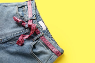 Sarı arka planda ölçü bandı olan kot pantolonlar. Anoreksi kavramı