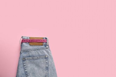 Pembe arka planda mezurası olan şık kot pantolonlar. Anoreksi kavramı