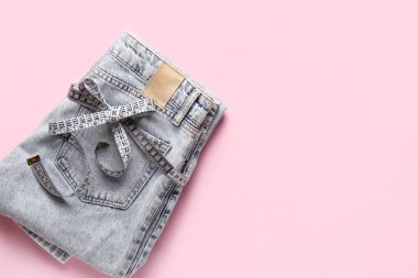 Pembe arka planda mezurası olan katlanmış kot pantolon. Anoreksi kavramı