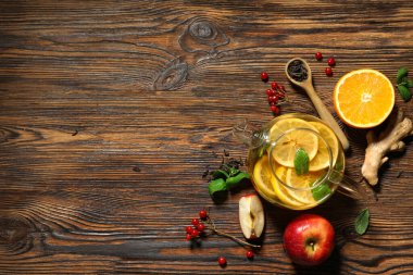 Cam çaydanlık dolusu lezzetli meyve çayı ve ahşap zemin üzerindeki malzemelerle kompozisyon.