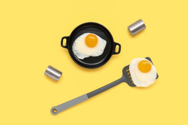Kızartma tavası ve spatula ile sarı arka planda lezzetli kızarmış yumurta.