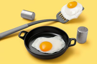 Kızartma tavası ve spatula ile sarı arka planda lezzetli sahanda yumurta, yakın plan.