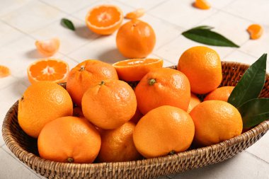 Tatlı mandalinalı hasır kase ve beyaz fayanslı yapraklar, yakın plan.