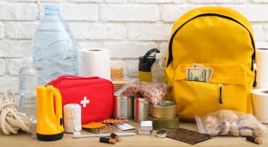 Acil durum çantası için gereksinimler beyaz tuğla duvarın yanındaki ahşap masada.