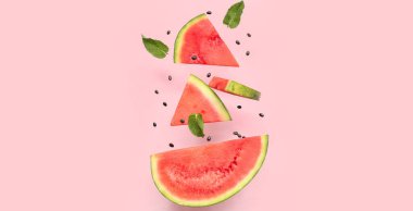 Uçan taze karpuz parçaları, pembe arka planda nane ve tohumlar