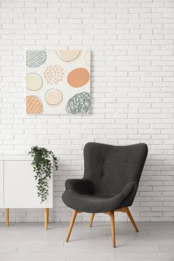 Koyu gri koltuk, şifonyeri, boyası ve beyaz tuğla duvarın yanındaki bitki örtüsü.