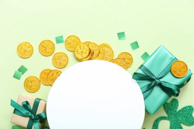 Blank round card with gifts, golden coins and paper decor on light green background. St. Patrick's Day celebration