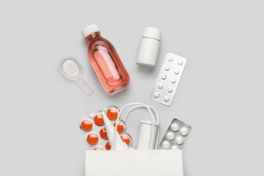 Üzerinde farklı haplar ve gri arka planda ilaç şişeleri olan kağıt torba.