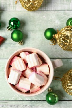 Bir fincan kremalı sıcak çikolata ve yeşil ahşap arka planda Noel topları.