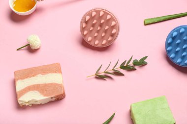 Saç derisi masaj aletleri, şampuan barları ve pembe arka planda bir kase bal.