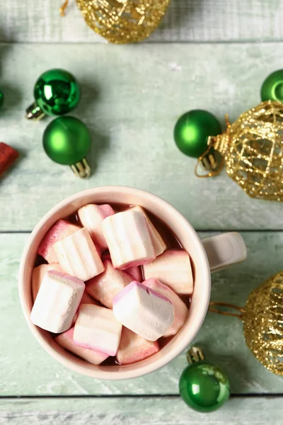 Bir fincan kremalı sıcak çikolata ve yeşil ahşap arka planda Noel topları.